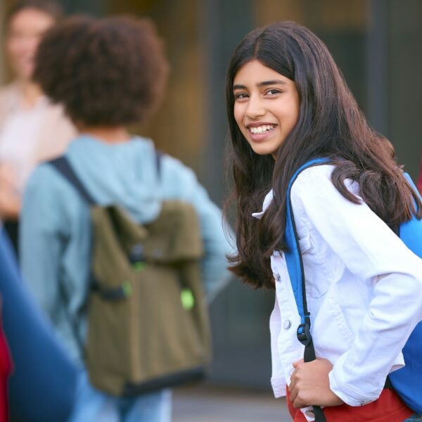 Portrait Of Female Secondary Or High School Student Outside School Building With Teachers And Pupils